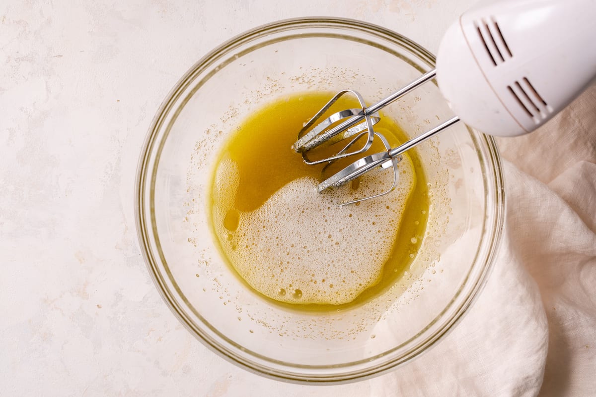 mixing bowl with olive oil, sugar, and aquafaba and electric mixer