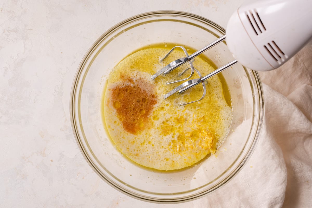 mixing bowl with olive oil, sugar, aquafaba, buttermilk and lemon zest and electric mixer