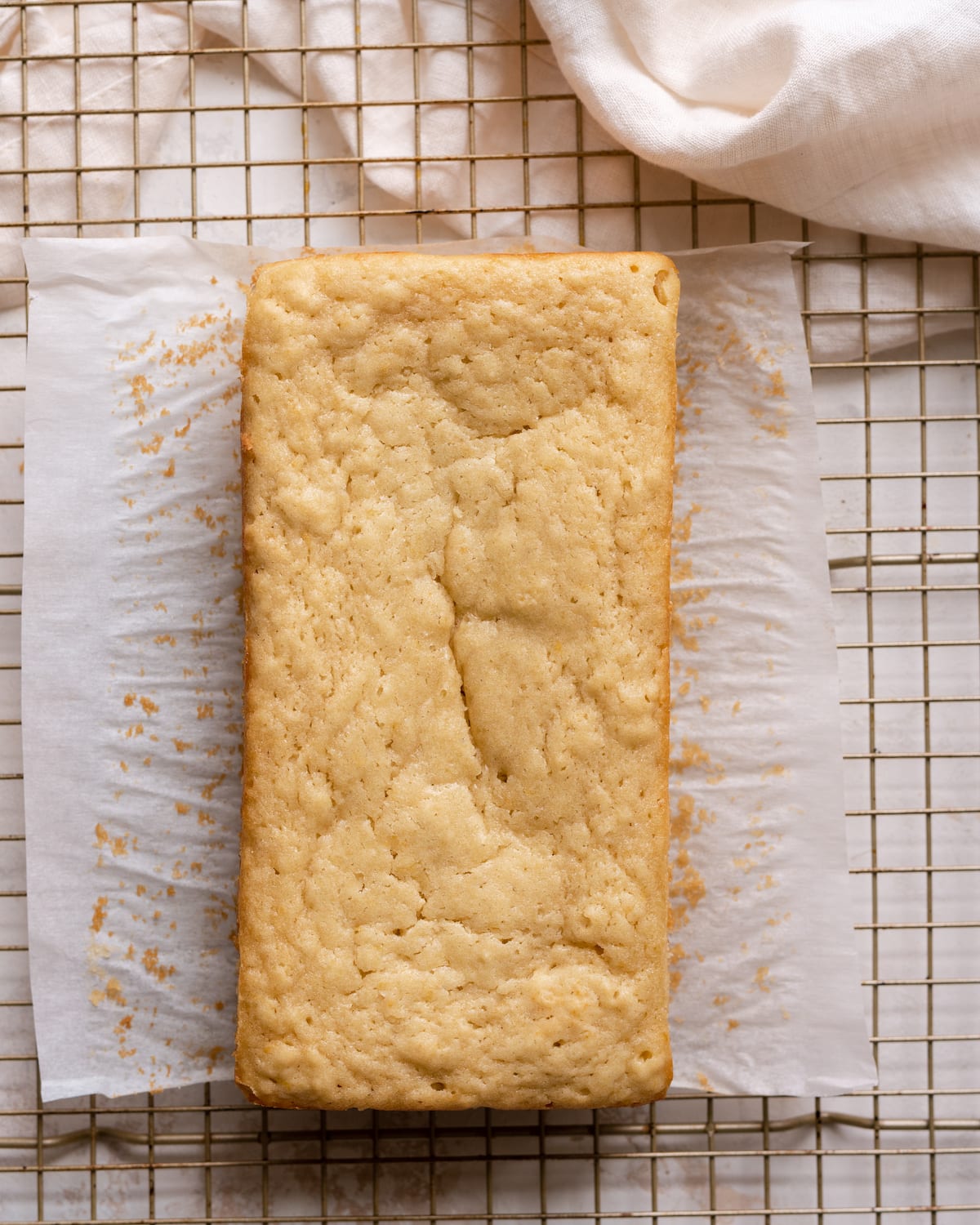 baked lemon olive oil cake on parchment paper on top of cooling wire rack