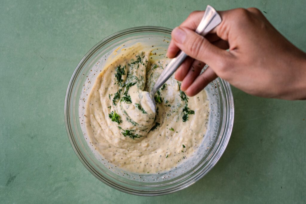 woman's hands whisking dill into potato salad dressing
