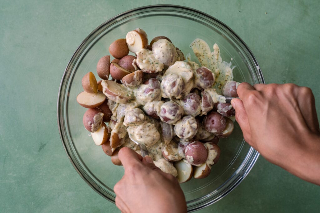 woman's hands tossing potatoes in dressing for vegan potato salad