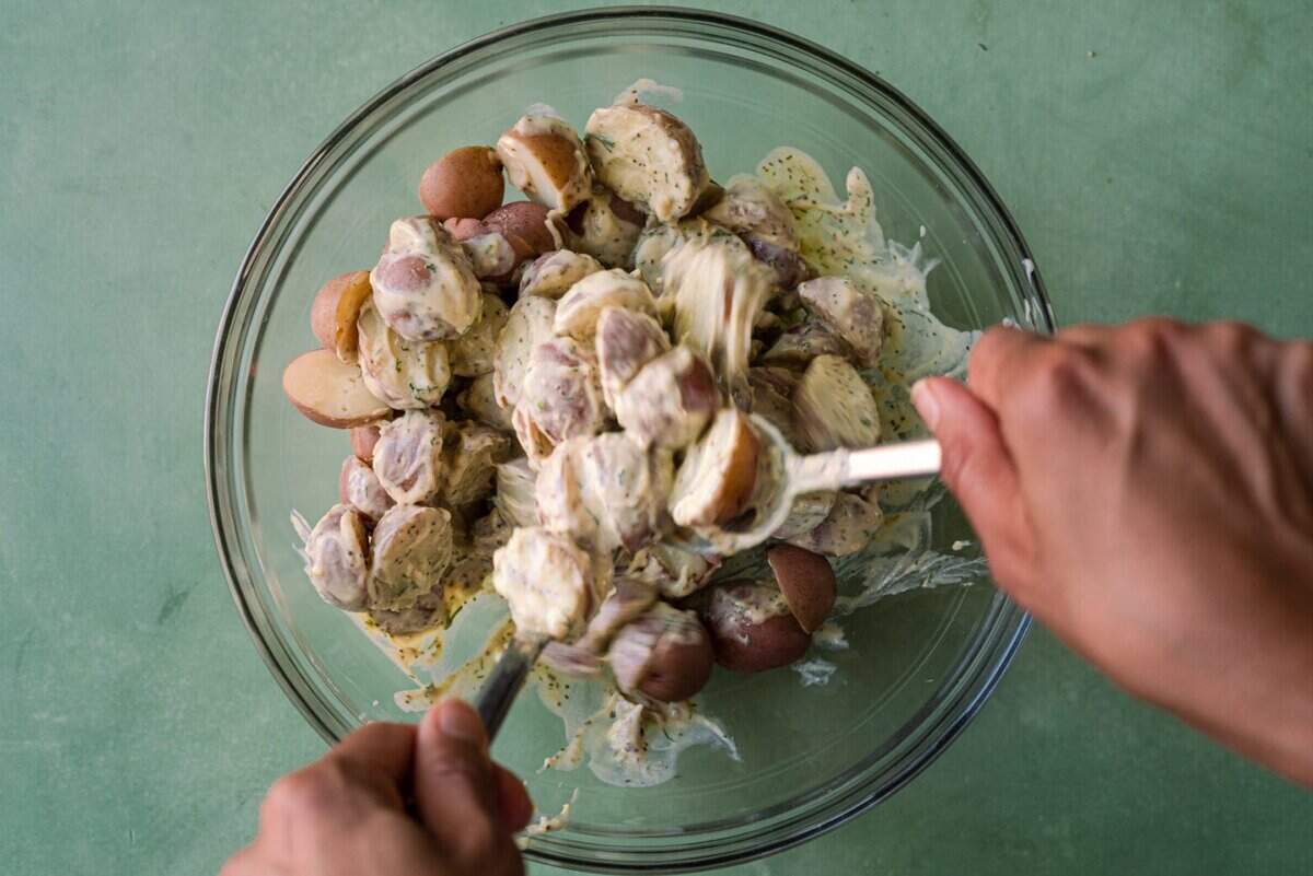 woman's hands tossing potatoes in dressing for vegan potato salad