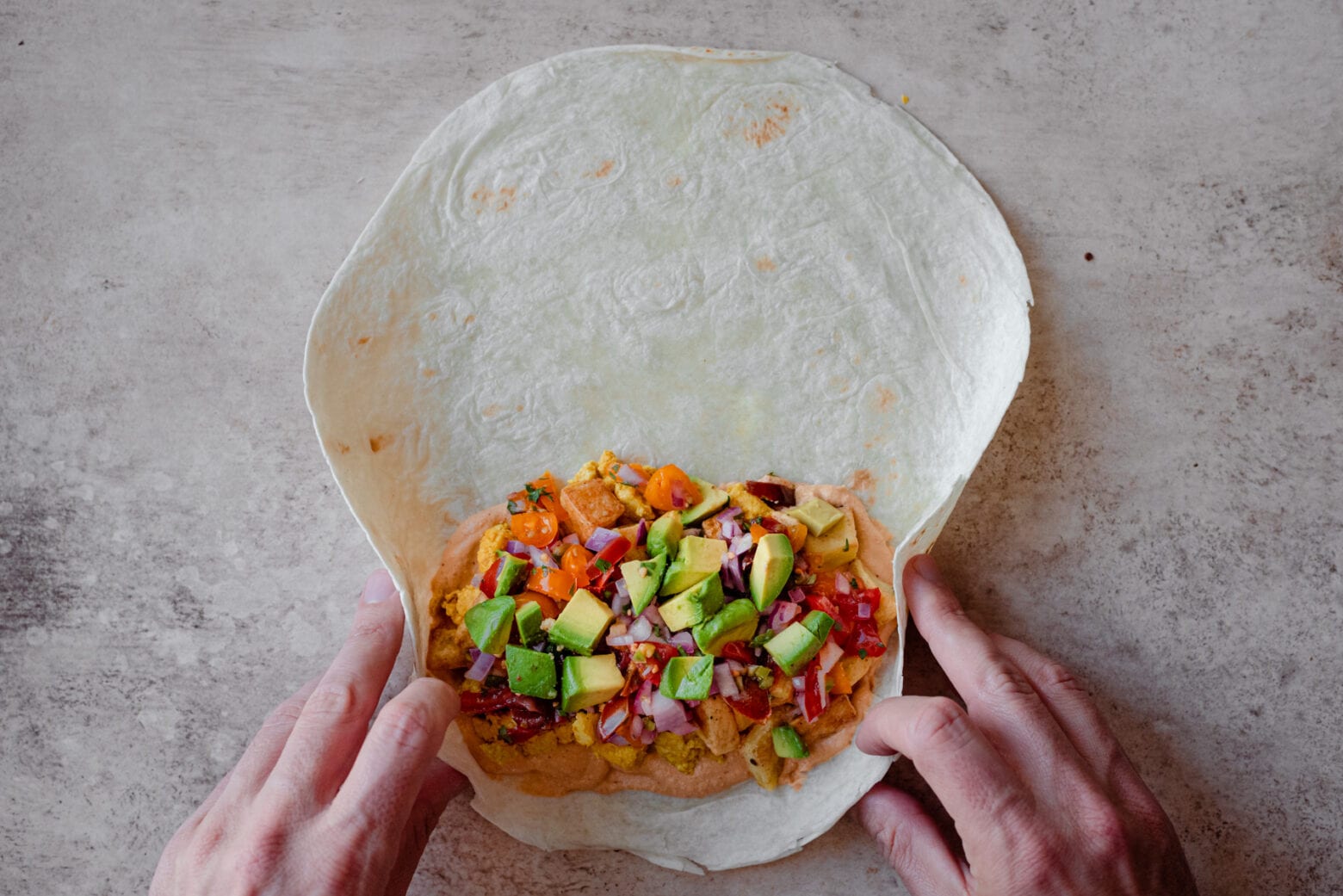 man's hands rolling up a vegan breakfast burrito
