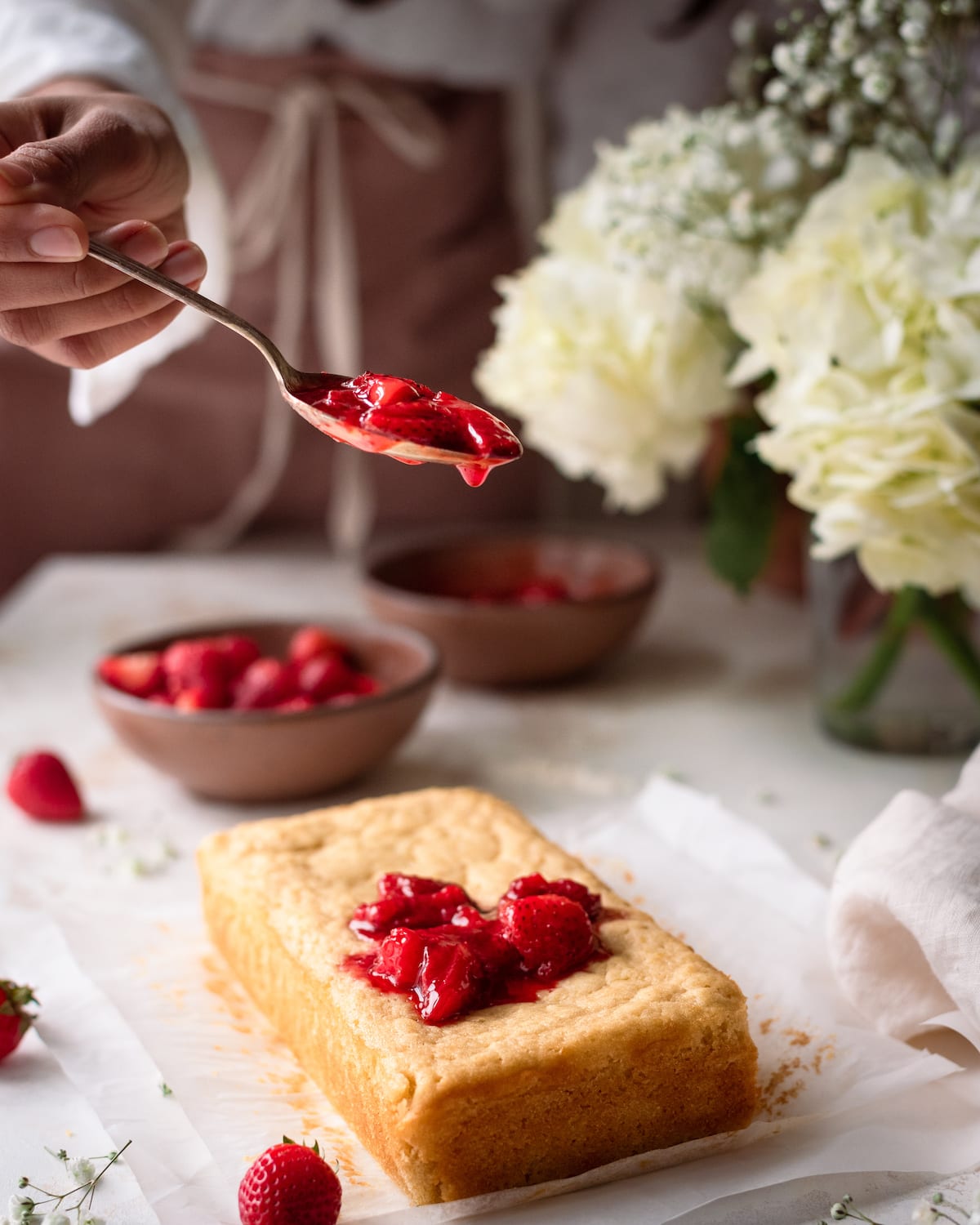 woman spooning strawberry sauce onto lemon olive oil cake in romantic food photography scene
