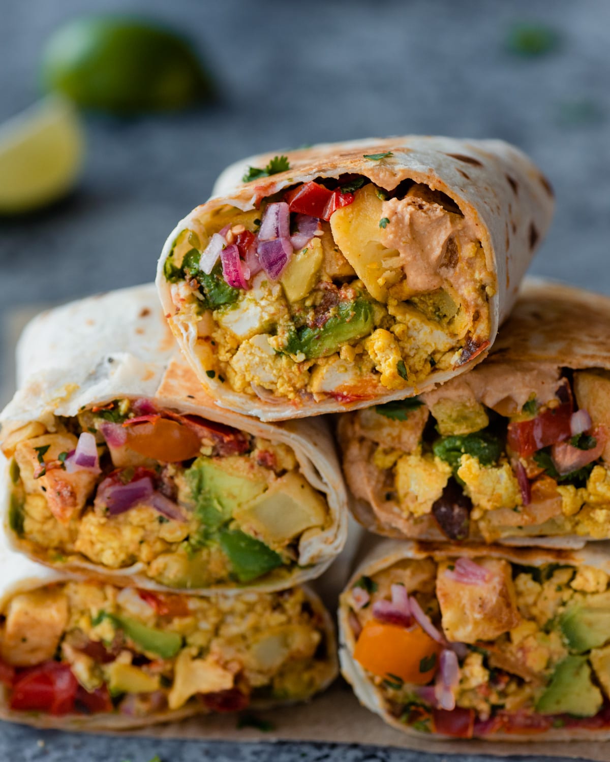 a closeup photo of a stack of vegan breakfast burritos on a blue backdrop