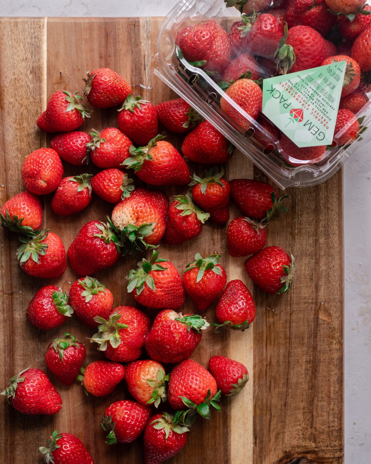 whole strawberries on wooden cutting board with package of strawberries