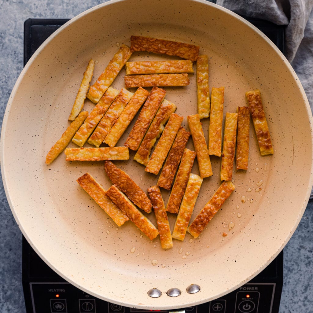 golden brown tempeh being cooked in frying pan