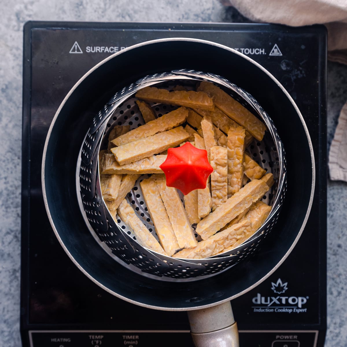 tempeh strips in steamer basket in a saucepan. 