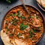 bowl of creamy vegan dal makhani with spoon and naan on blue background