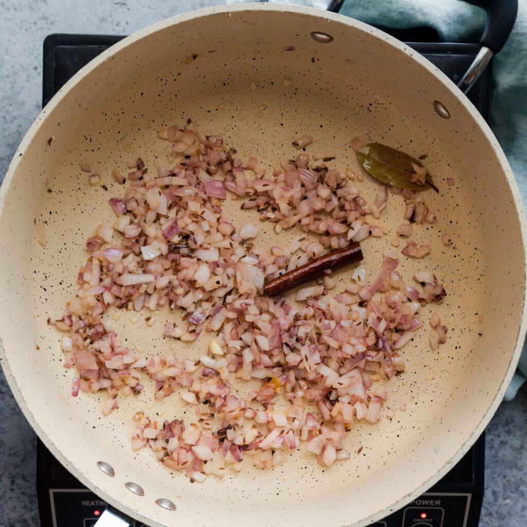 cooking red onions and whole spices in a frying pan