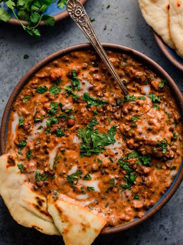 bowl of creamy vegan dal makhani with spoon and naan on blue background