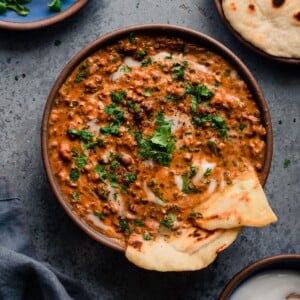 bowl of creamy vegan dal makhani with naan, yogurt, and cilantro on blue background