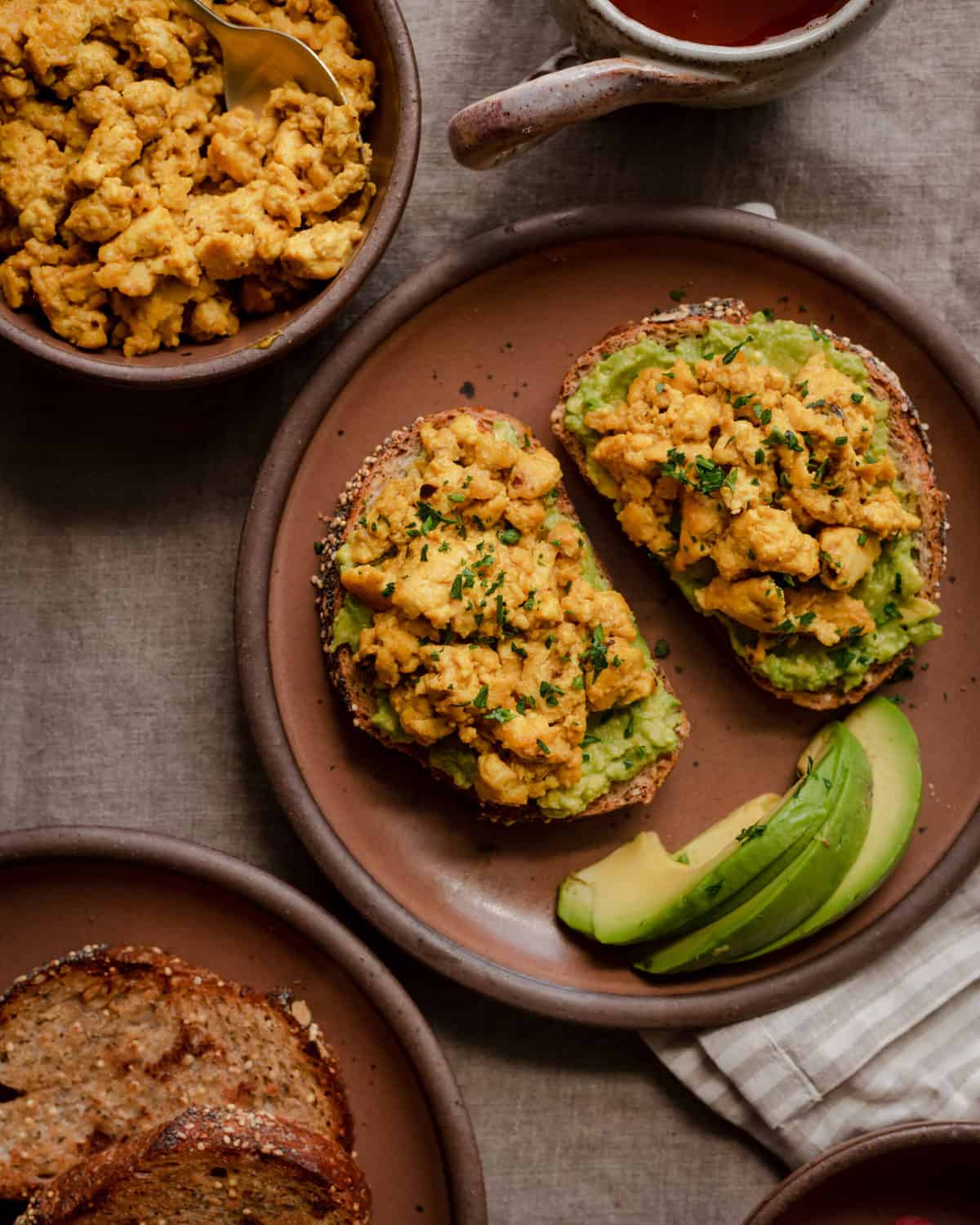 vegan tofu scramble on top of avocado toast on plate with side of tofu scramble on the side.