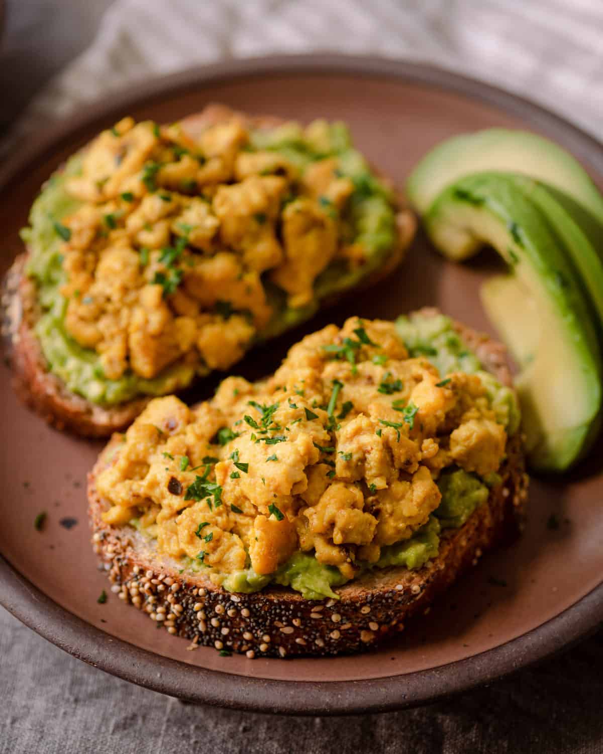 vegan tofu scramble on top of avocado toast on plate.