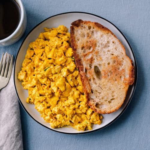 tofu scramble with toast on a plate next to a cup of coffee.