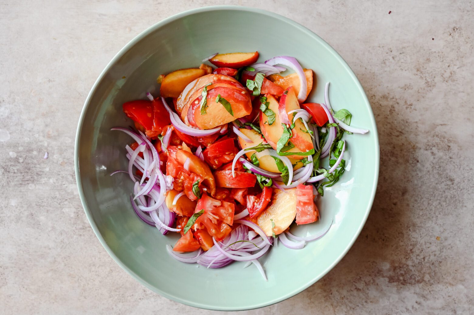 sliced peaches, tomatoes, onions, and basil in a large bowl for panzanella salad