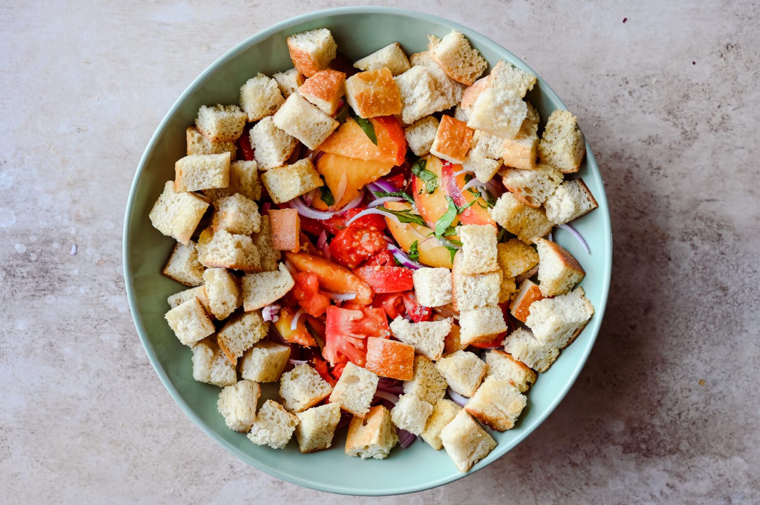 toasted bread cubes with sliced peaches, tomatoes, onions, and basil in a large bowl for panzanella salad