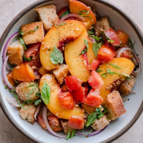 peach panzanella salad in a white bowl on a pink surface.
