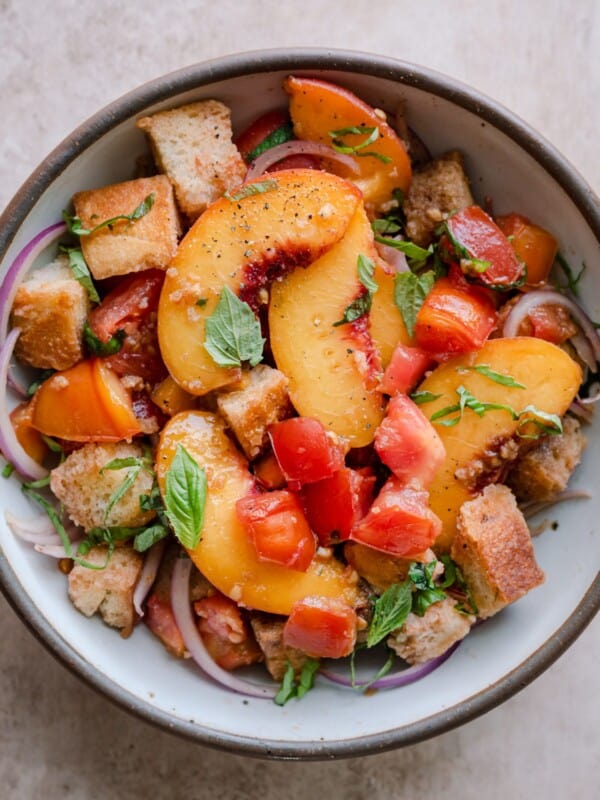 peach panzanella salad in a white bowl on a pink surface.