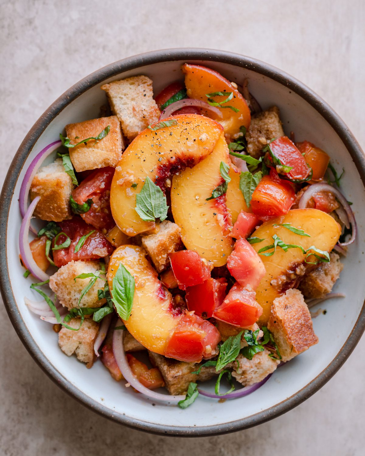 peach panzanella salad in a white bowl on a pink surface