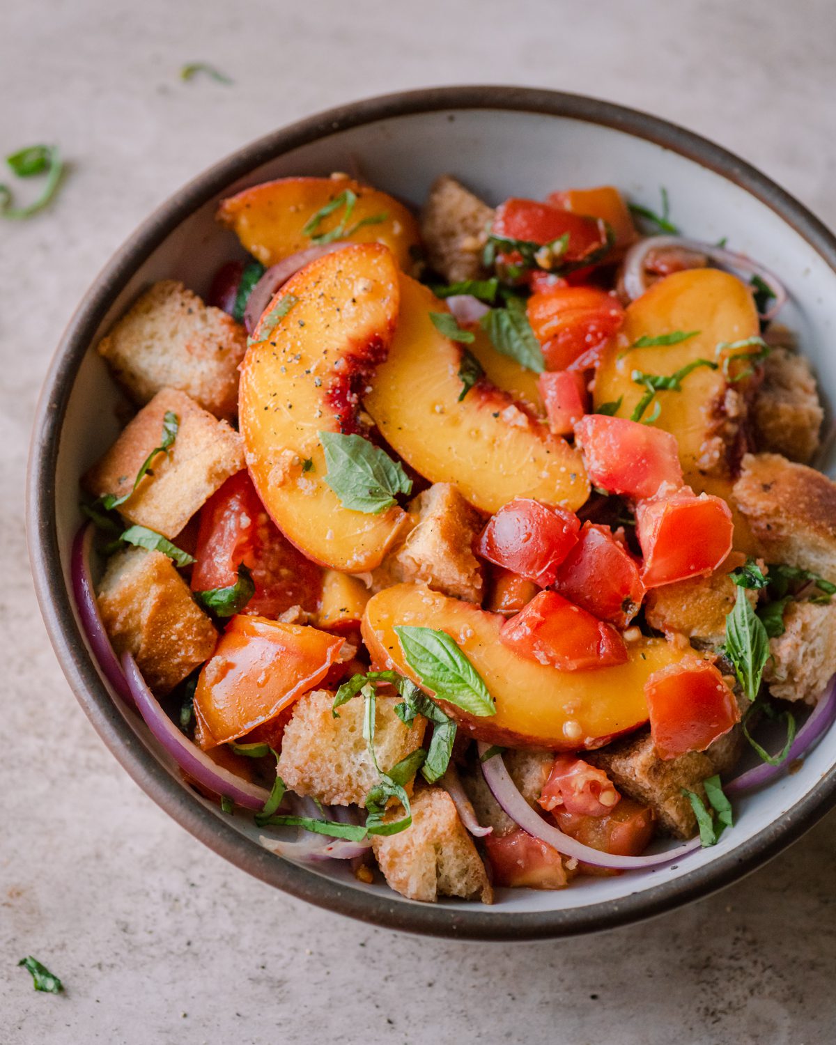 peach panzanella salad in a white bowl on a pink surface