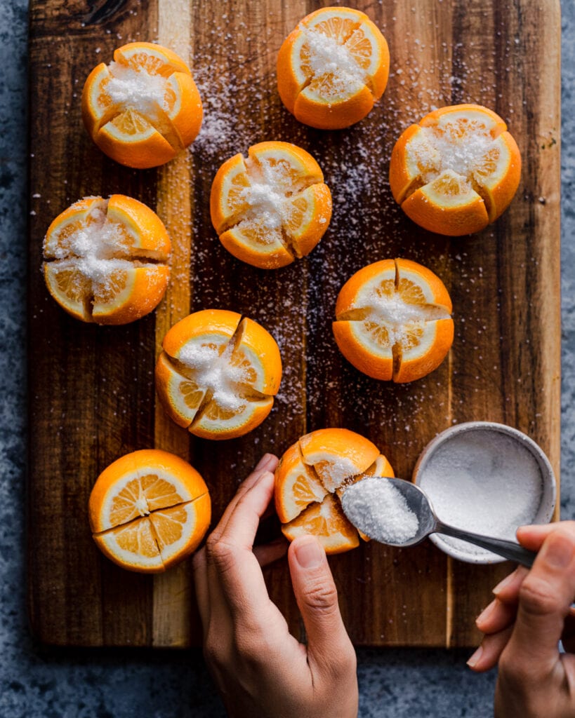 woman's hands spooning salt into sliced lemons for preserved lemons