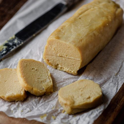 log of cashew cheese on parchment paper with knife.