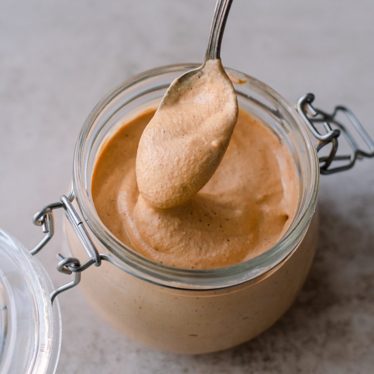 vegan queso spooned from a glass jar on a table.