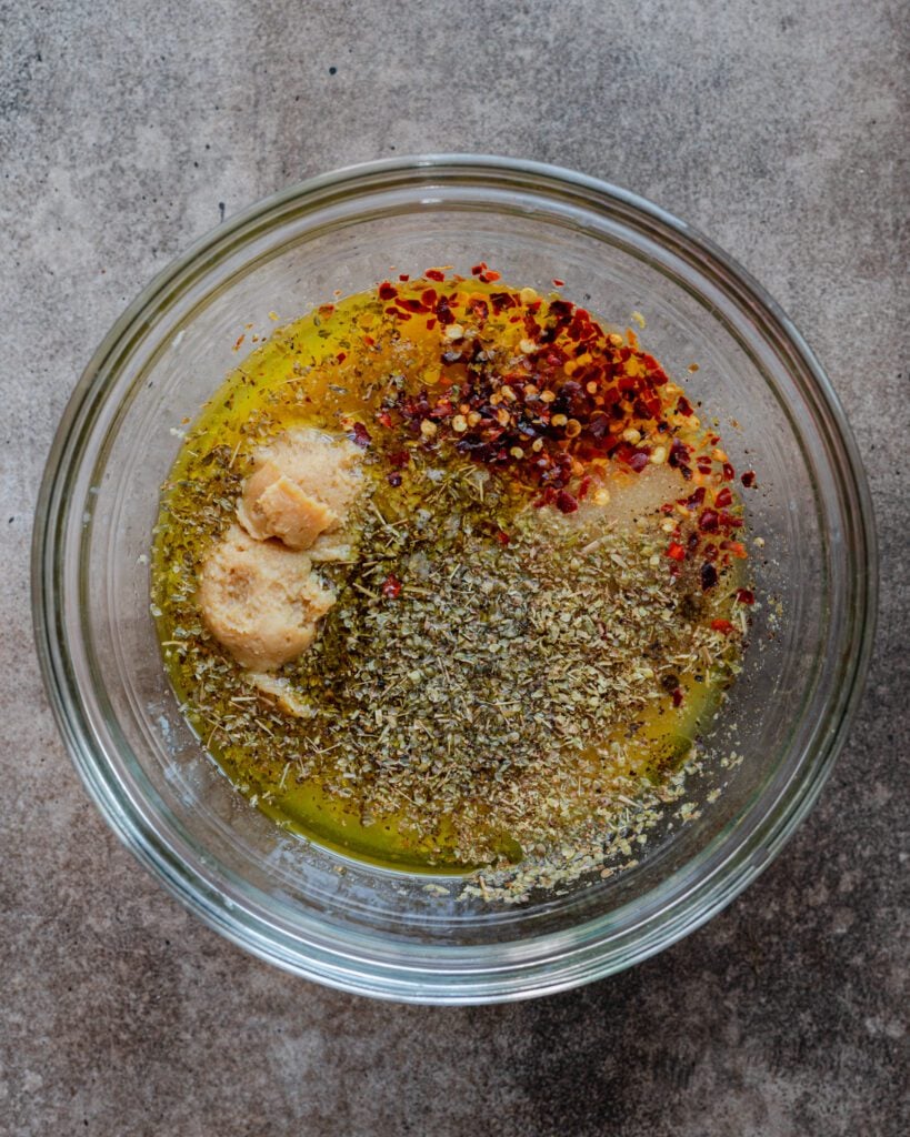 ingredients for the marinade to a medium bowl: miso paste, apple cider vinegar, olive oil, lemon juice, garlic, nutritional yeast, spices, and salt/pepper