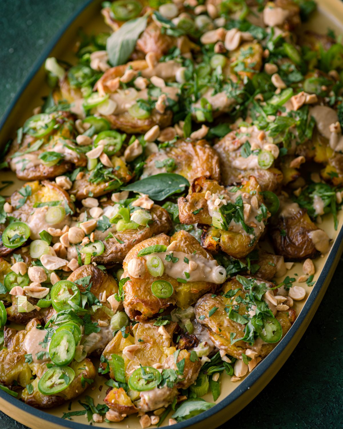 crispy smashed potatoes with ginger-tahini dressing, scallions, herbs, and peanuts