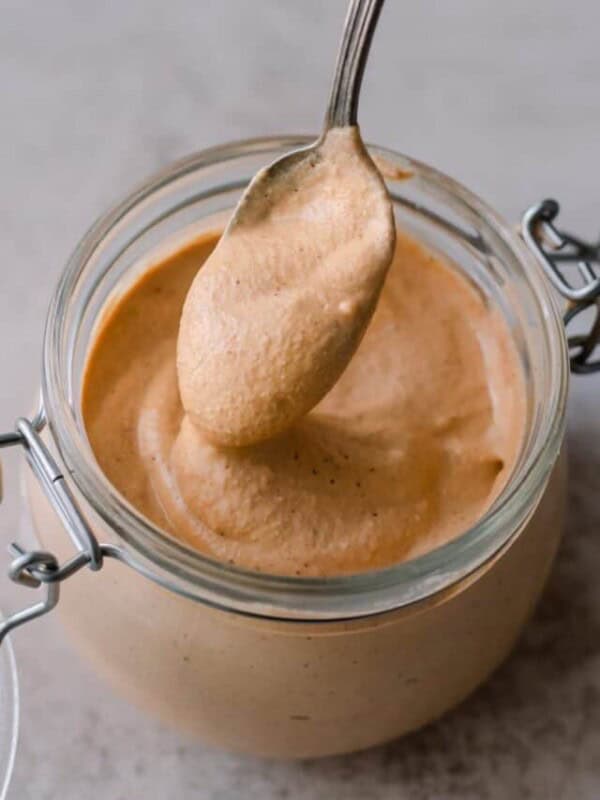vegan queso spooned from a glass jar on a table.
