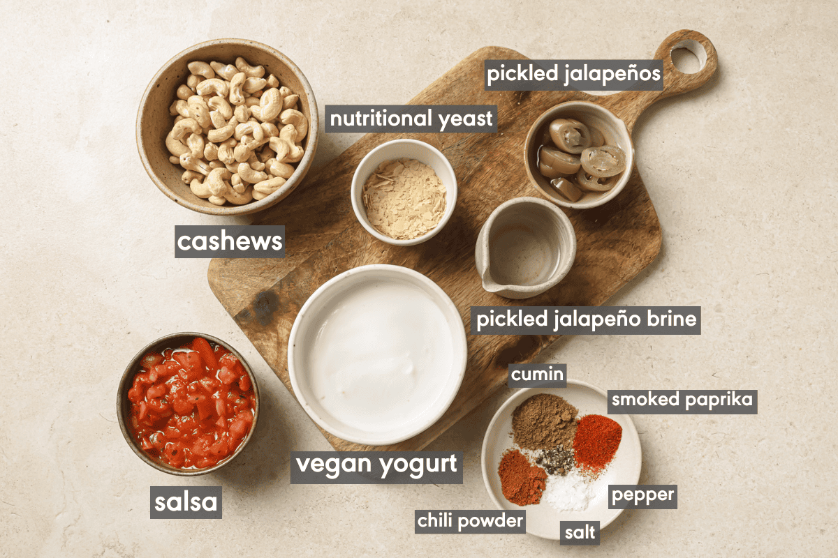vegan queso ingredients in various small bowls on a wooden cutting board.