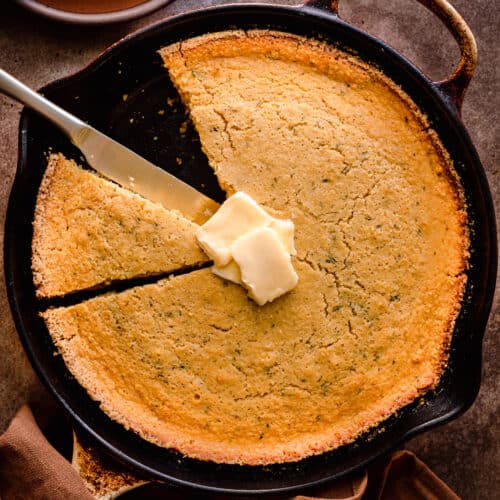vegan cornbread in a cast iron skillet with a slice taken out and vegan butter on top