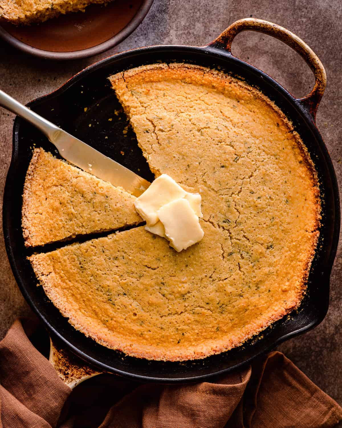 vegan cornbread in a cast iron skillet with a slice taken out and vegan butter on top