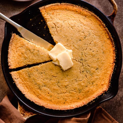 vegan cornbread in a cast iron skillet with a slice taken out and vegan butter on top