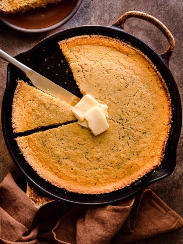 vegan cornbread in a cast iron skillet with a slice taken out and vegan butter on top