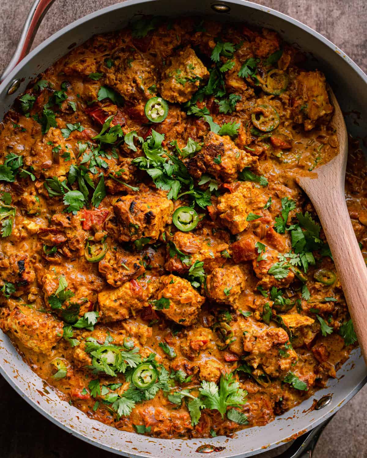 tofu tikka masala in a saute pan, garnished with cilantro and green chili peppers