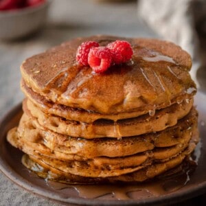 vegan pumpkin pancakes with maple syrup and raspberries on linen tablecloth