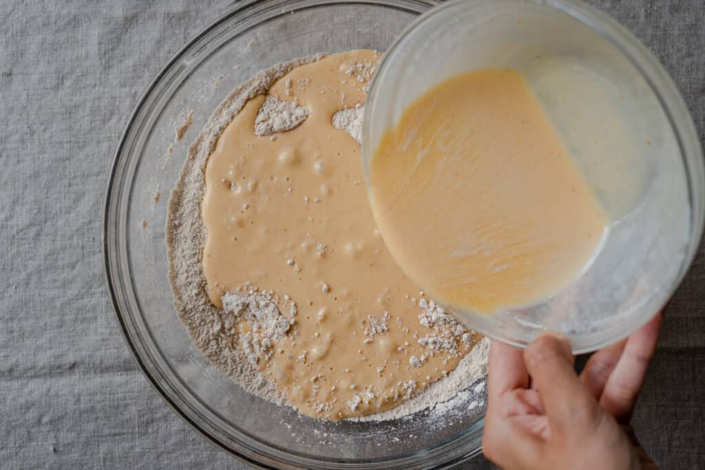 woman's hands pouring liquid ingredients into bowl of flour