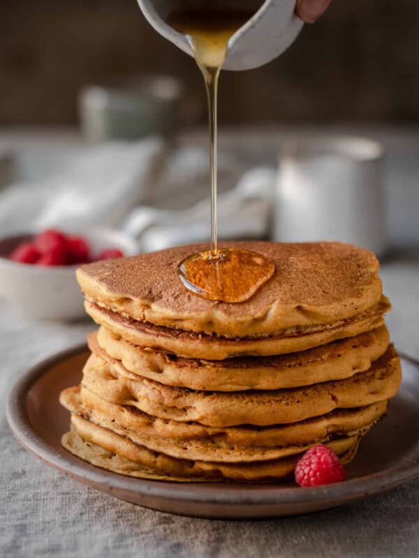 action shot of pouring maple syrup onto a stack of vegan pumpkin pancakes