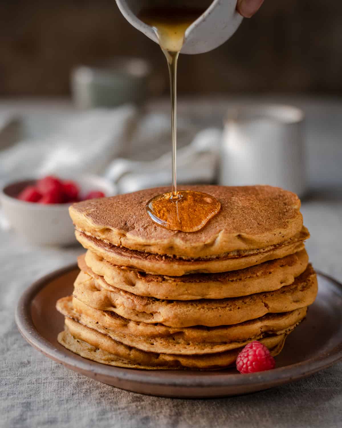 action shot of pouring maple syrup onto a stack of vegan pumpkin pancakes