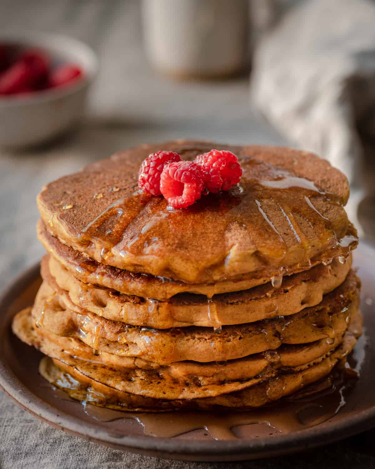 vegan pumpkin pancakes with maple syrup and raspberries on linen tablecloth