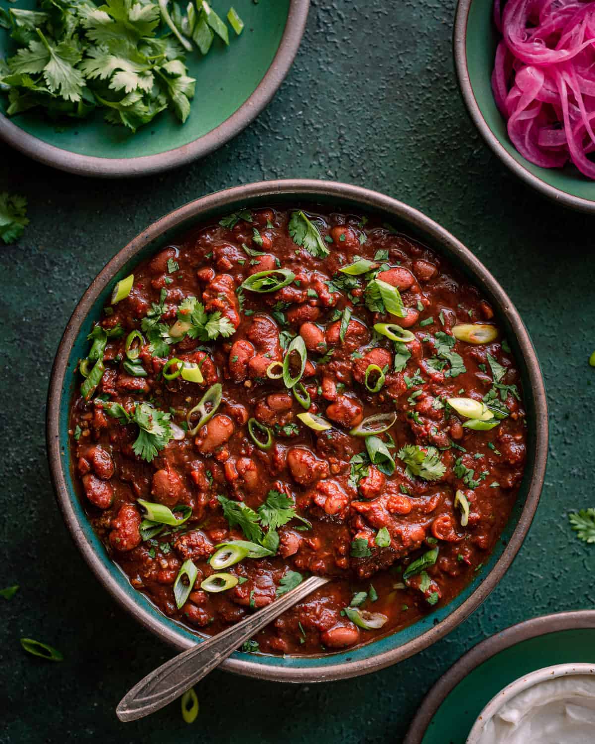 vegan chili on green surface with cilantro and pickled onions