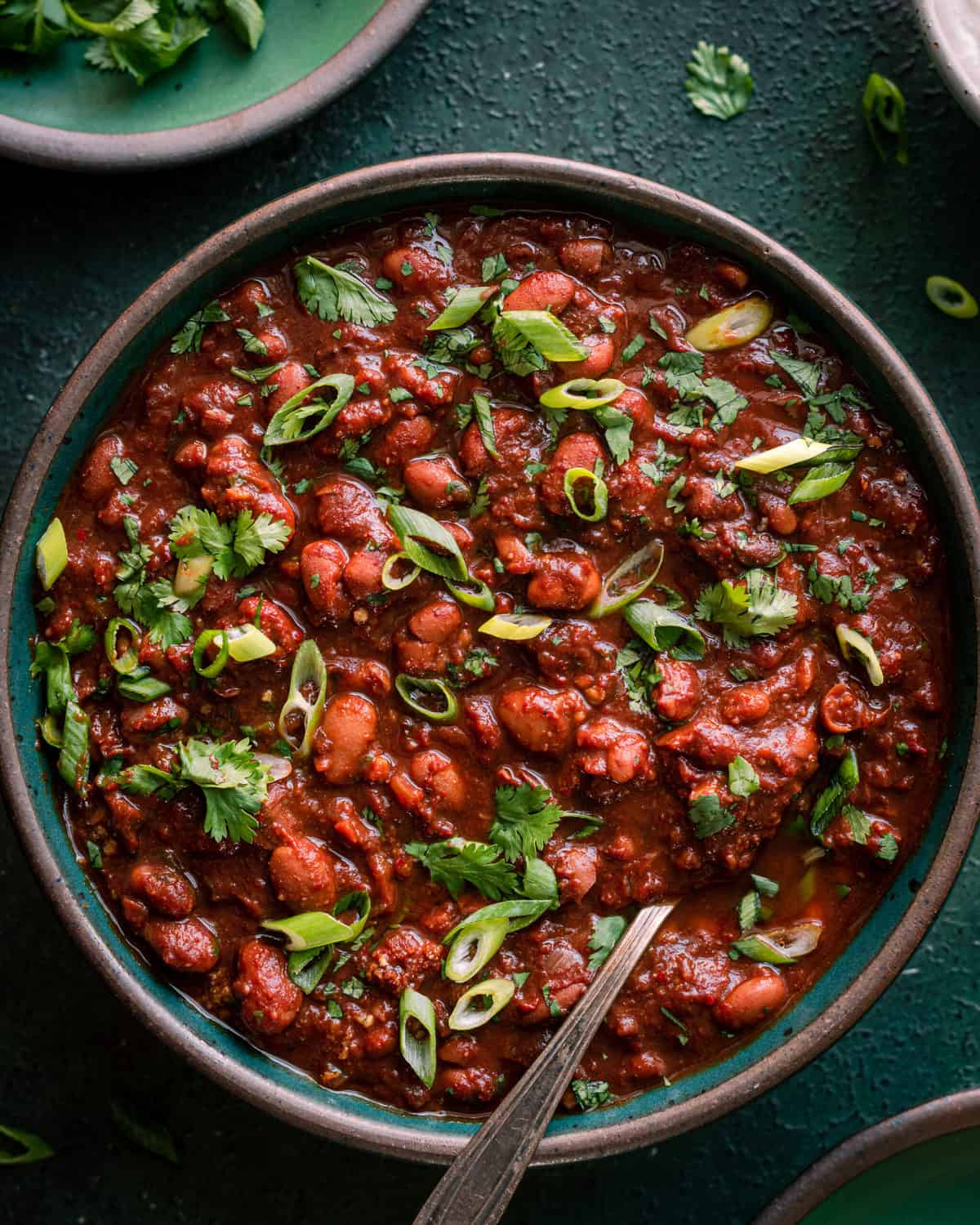 bowl of vegetarian chili on green surface with cilantro and scallions