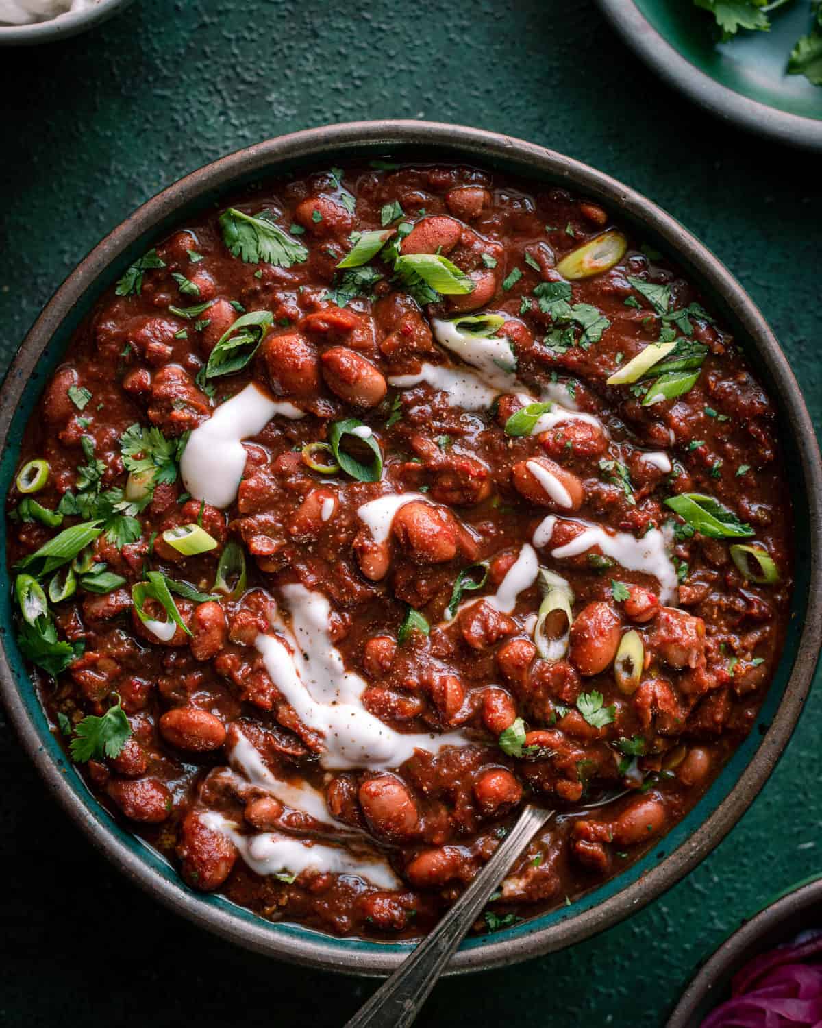 bowl of vegetarian chili on green backgrop with pickled onions and sour cream