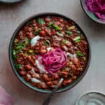 bowl of vegan chili with sour cream, cilantro and pickled onions