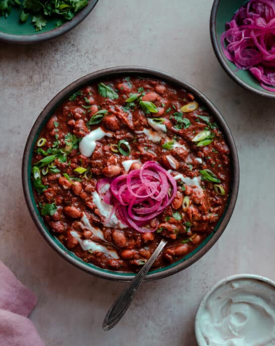 bowl of vegan chili with sour cream, cilantro and pickled onions