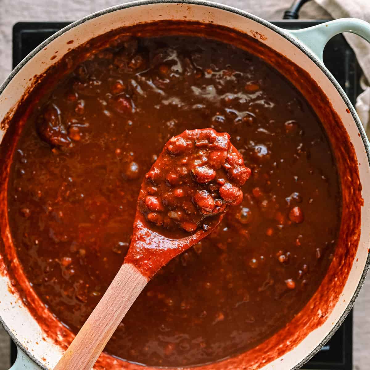 wooden spoon scooping from the pot of finished vegan chili.