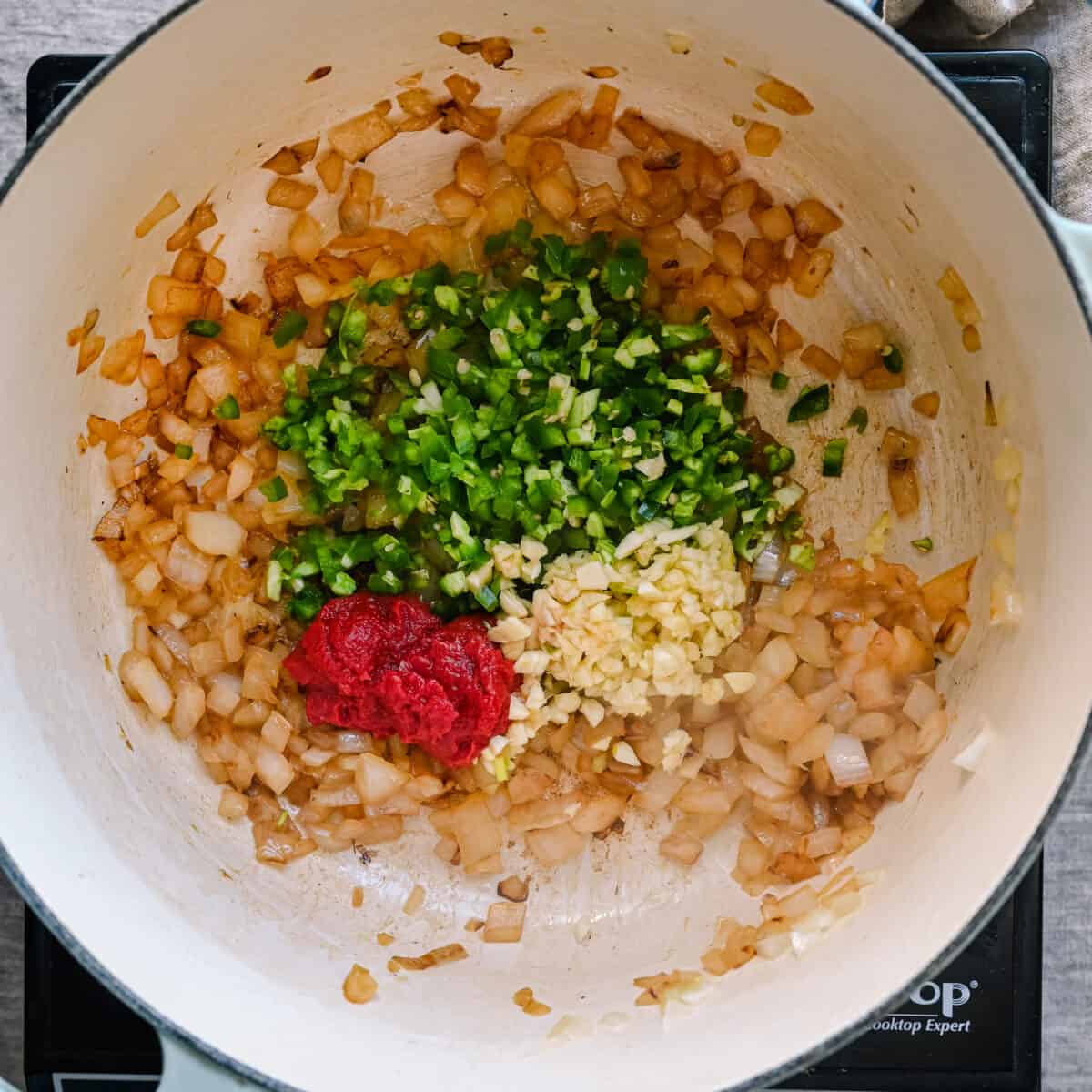 garlic, tomato paste, and jalapenos sitting on top of browned onions in a dutch oven