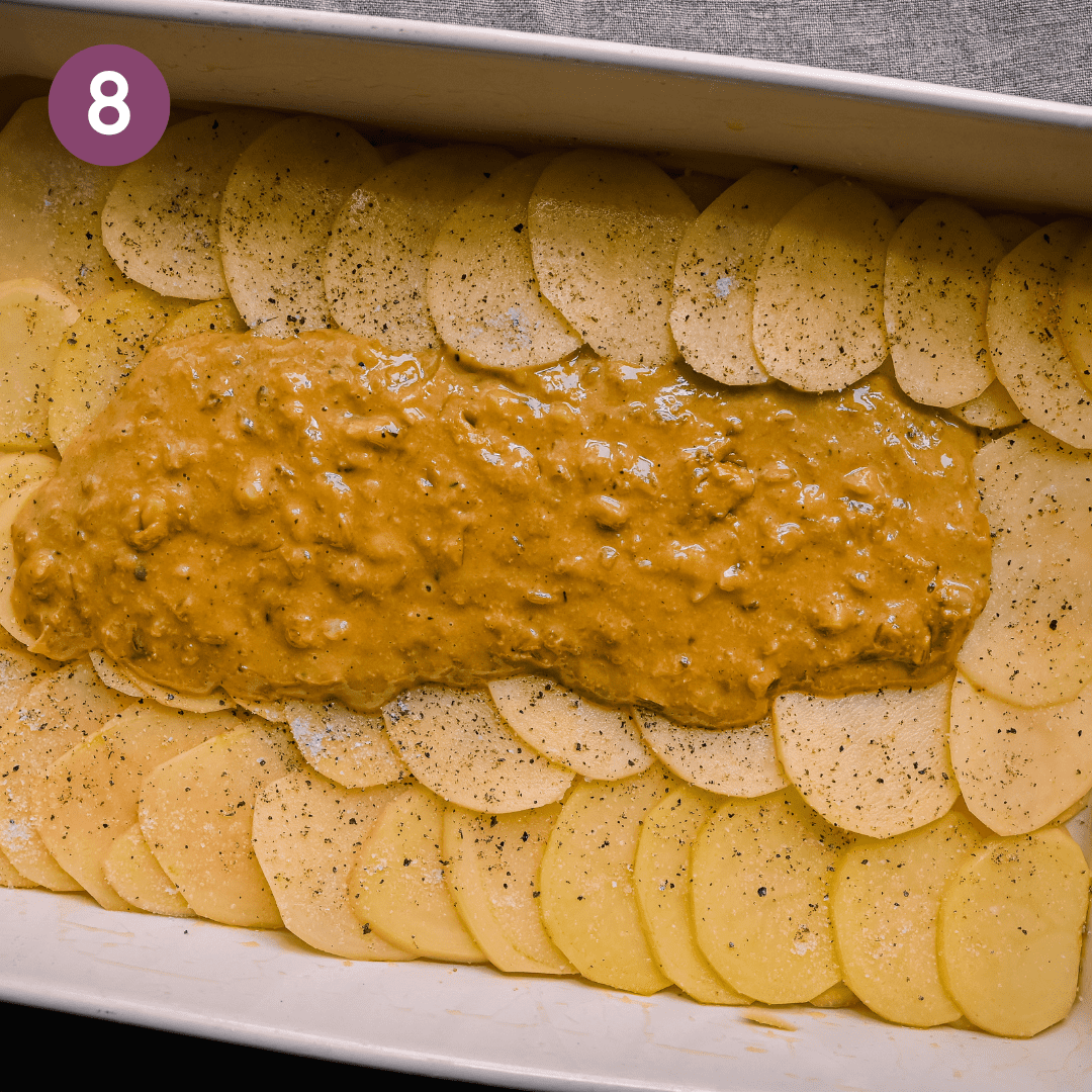 sliced potatoes overlapping in a casserole pan with cheesy sauce on top for scalloped potatoes